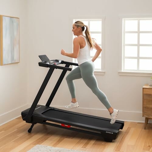 Woman jogging on a treadmill in a bright room.